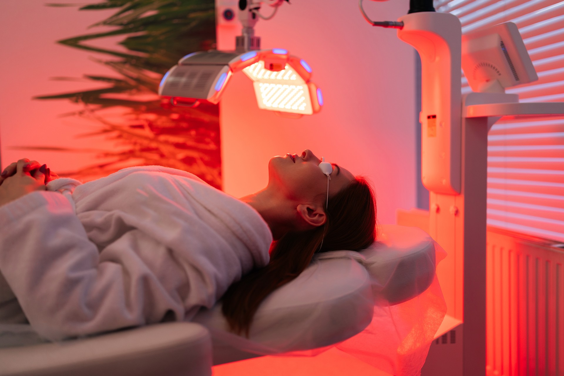 Side view of female patient undergoes red LED light or RLT therapy for skin rejuvenation at modern luxury aesthetic clinic. Young brunette woman client